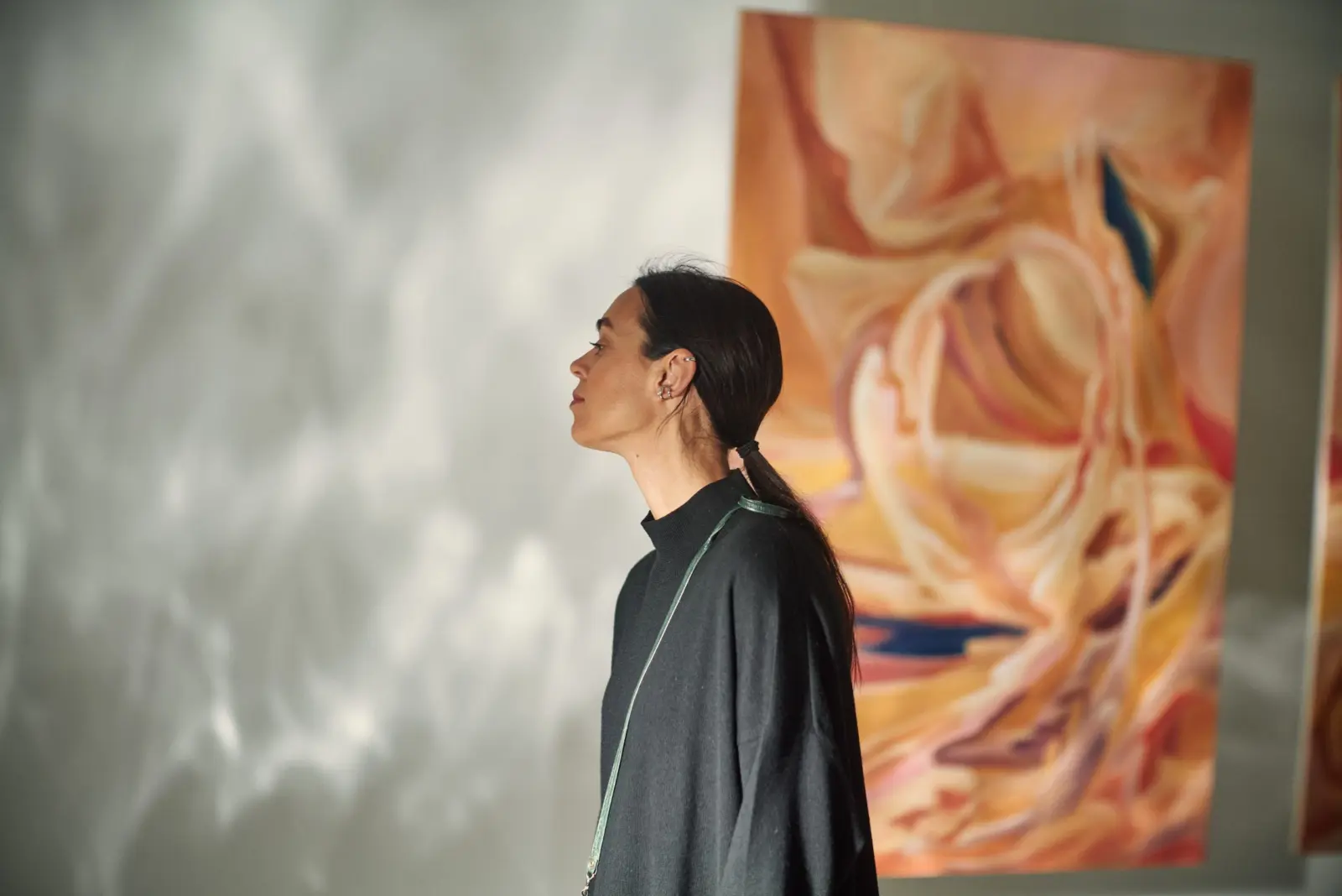 A visitor in patterned sunlight beside a painting at Dimension of the Heart