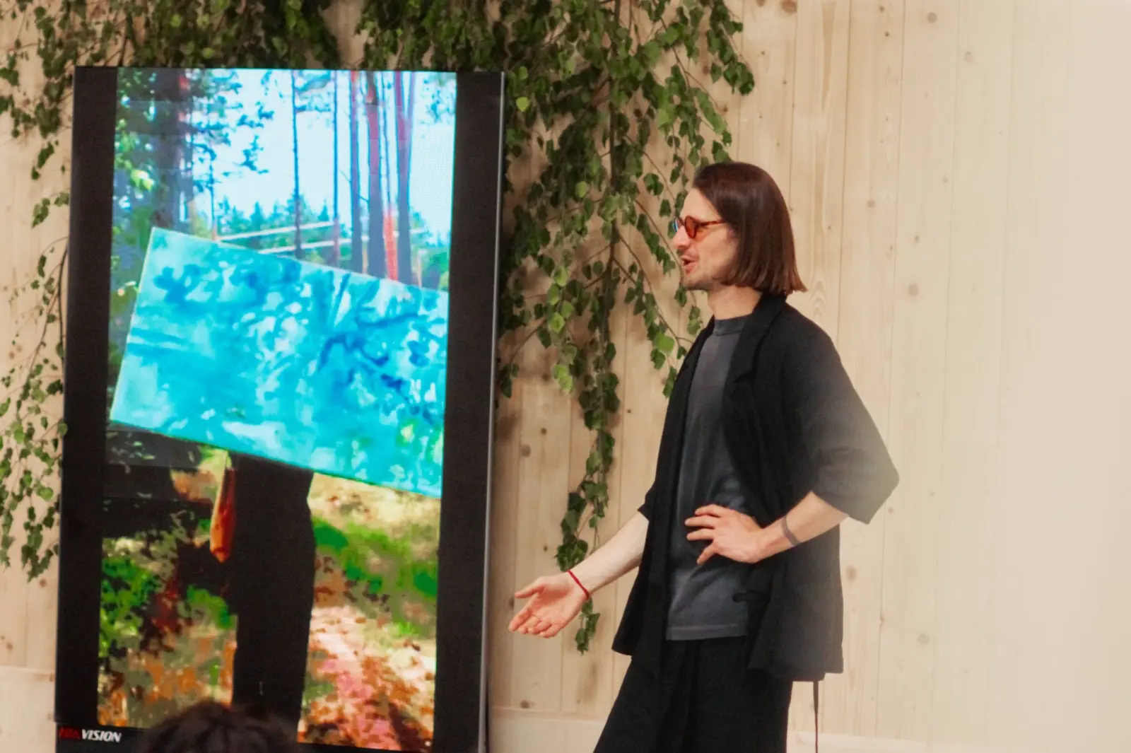 A speaker presenting beside a forest video at Nuoramos